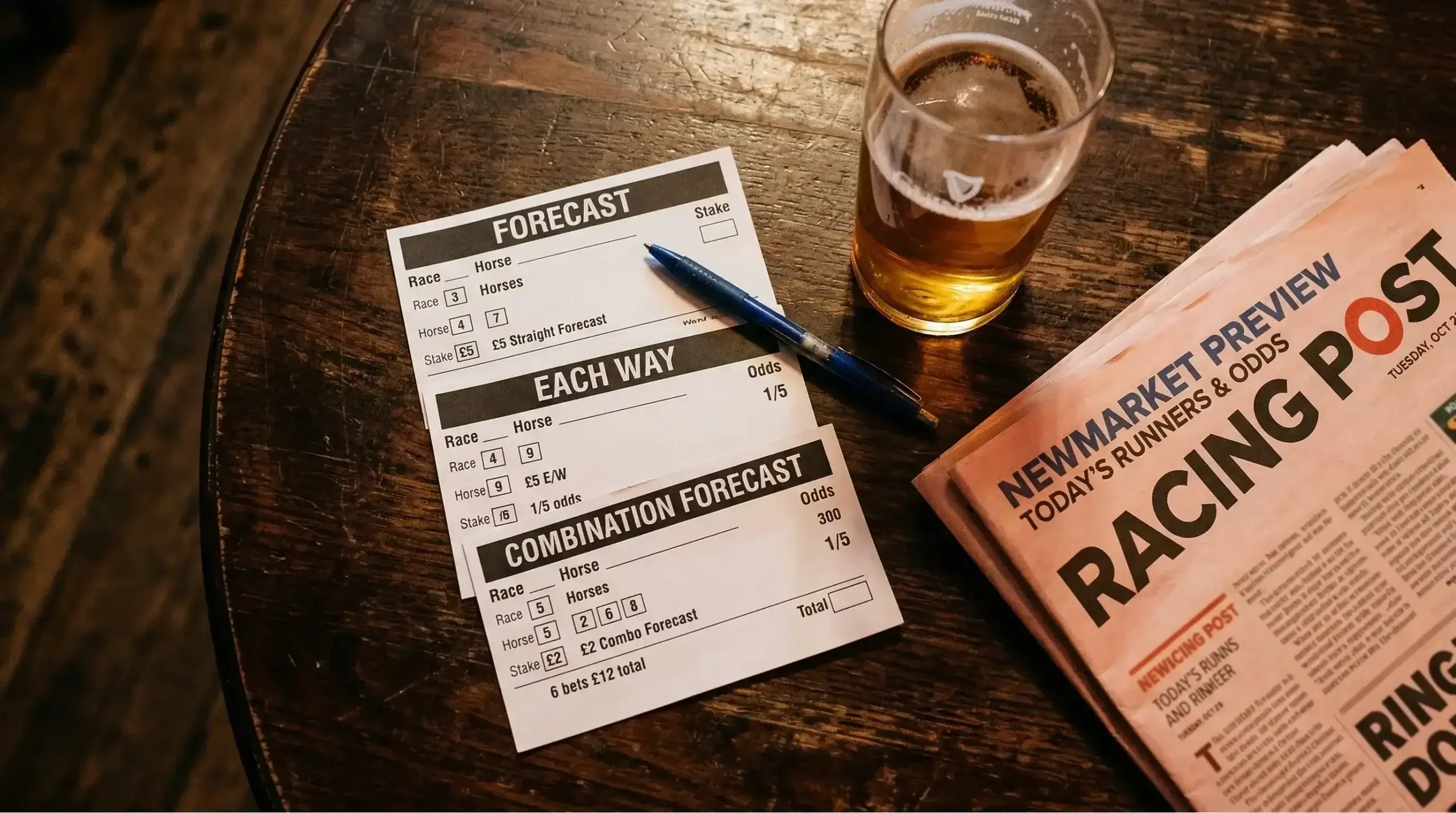 Betting slips fanned out on a wooden surface beside a UK racecourse railing
